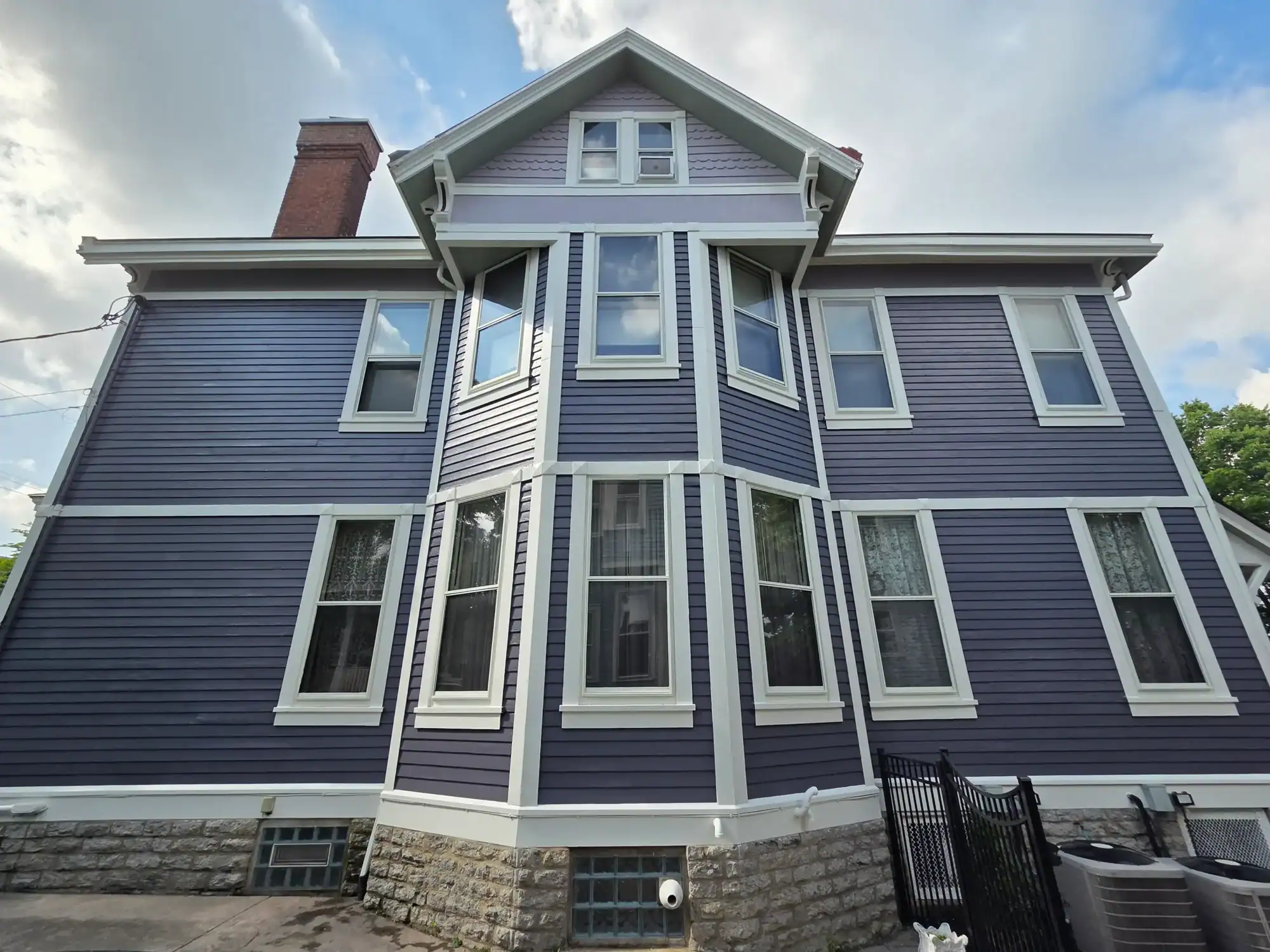 Professional exterior painting Hamilton - dark blue Victorian home with white trim and brick foundation